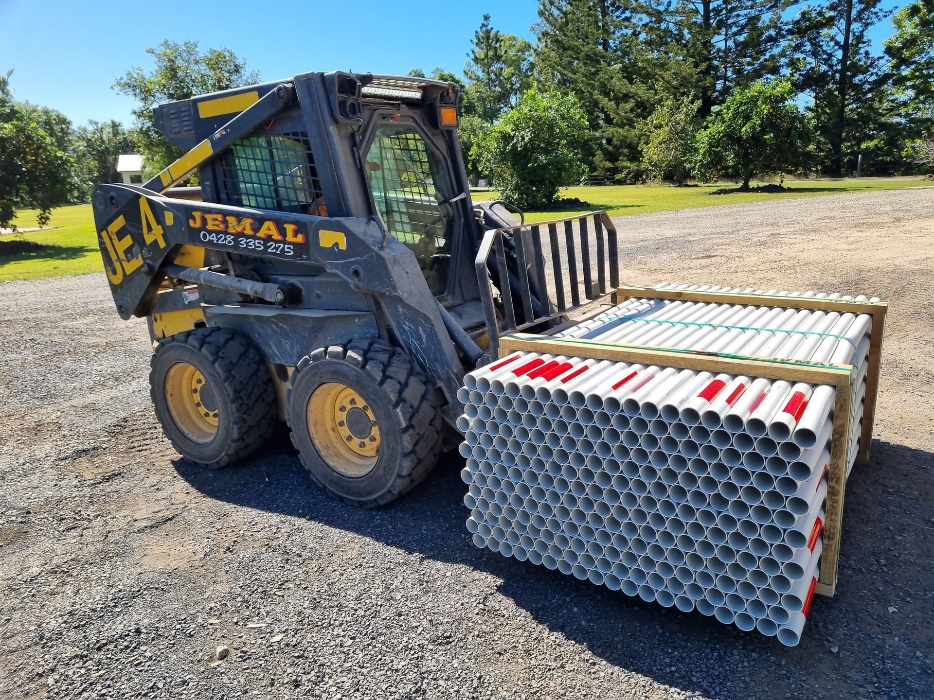 Skid Steer Loader Carrying a Large Pallet of White Tubes — Jemal Enterprises In Finch Hatton, QLD