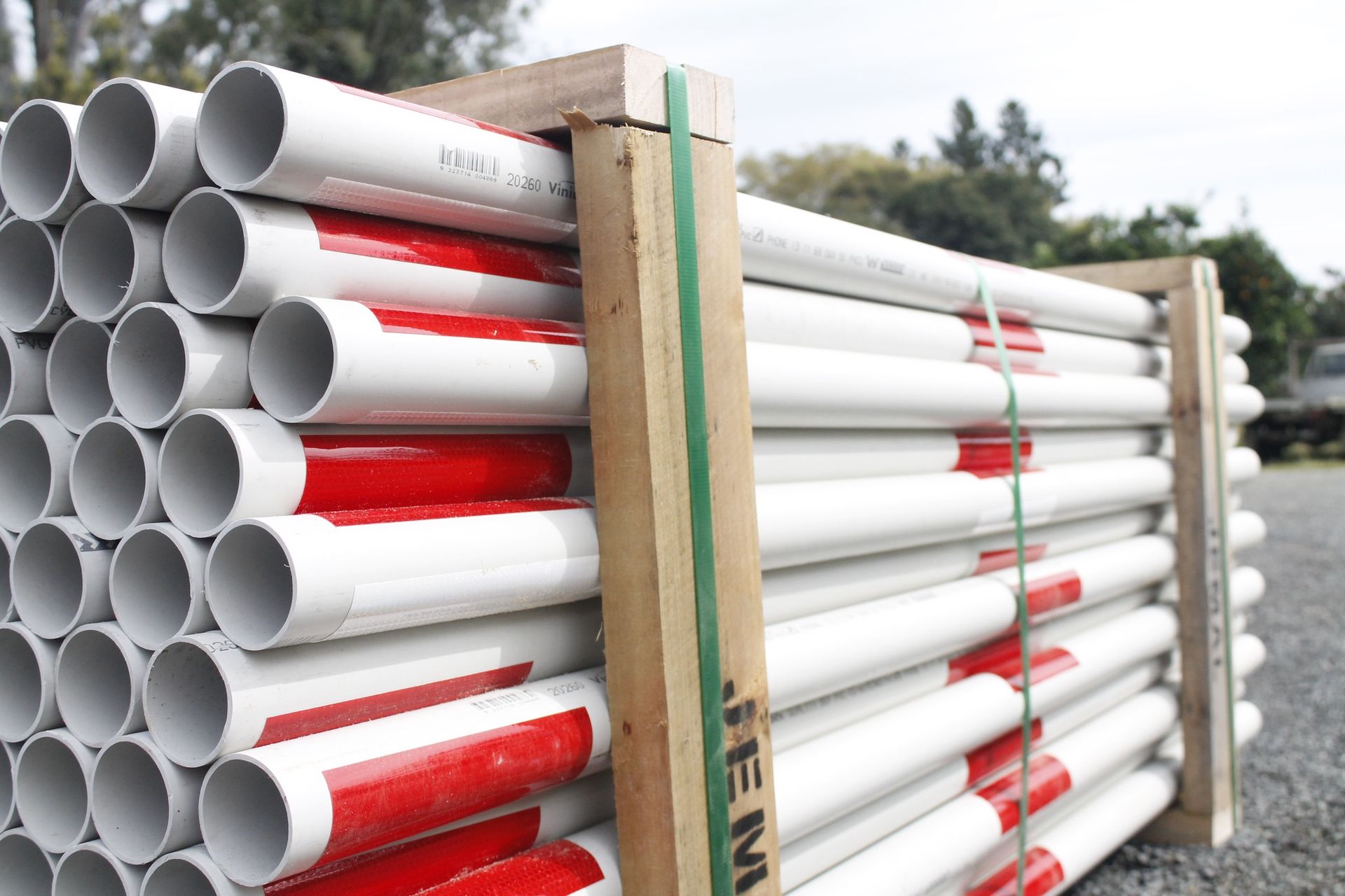 Bundle of white PVC pipes with red stripes, secured in a wooden frame with green strapping.