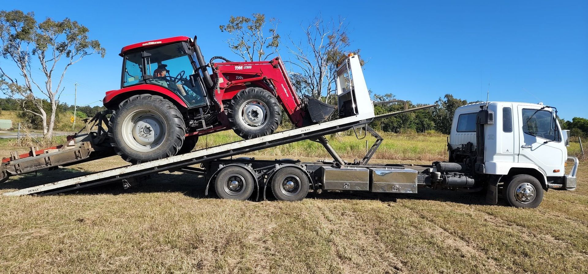 Red Tractor on a White Flatbed Truck in a Field — Jemal Enterprises In Finch Hatton, QLD