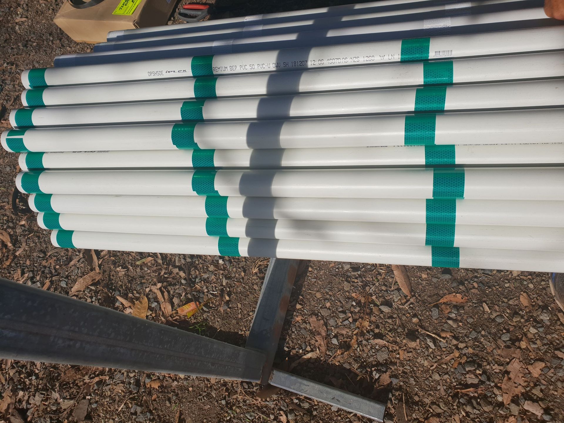 A stack of white PVC pipes with evenly spaced green tape stripes, resting on a metal stand outdoors on gravel  — Jemal Enterprises In Finch Hatton, QLD