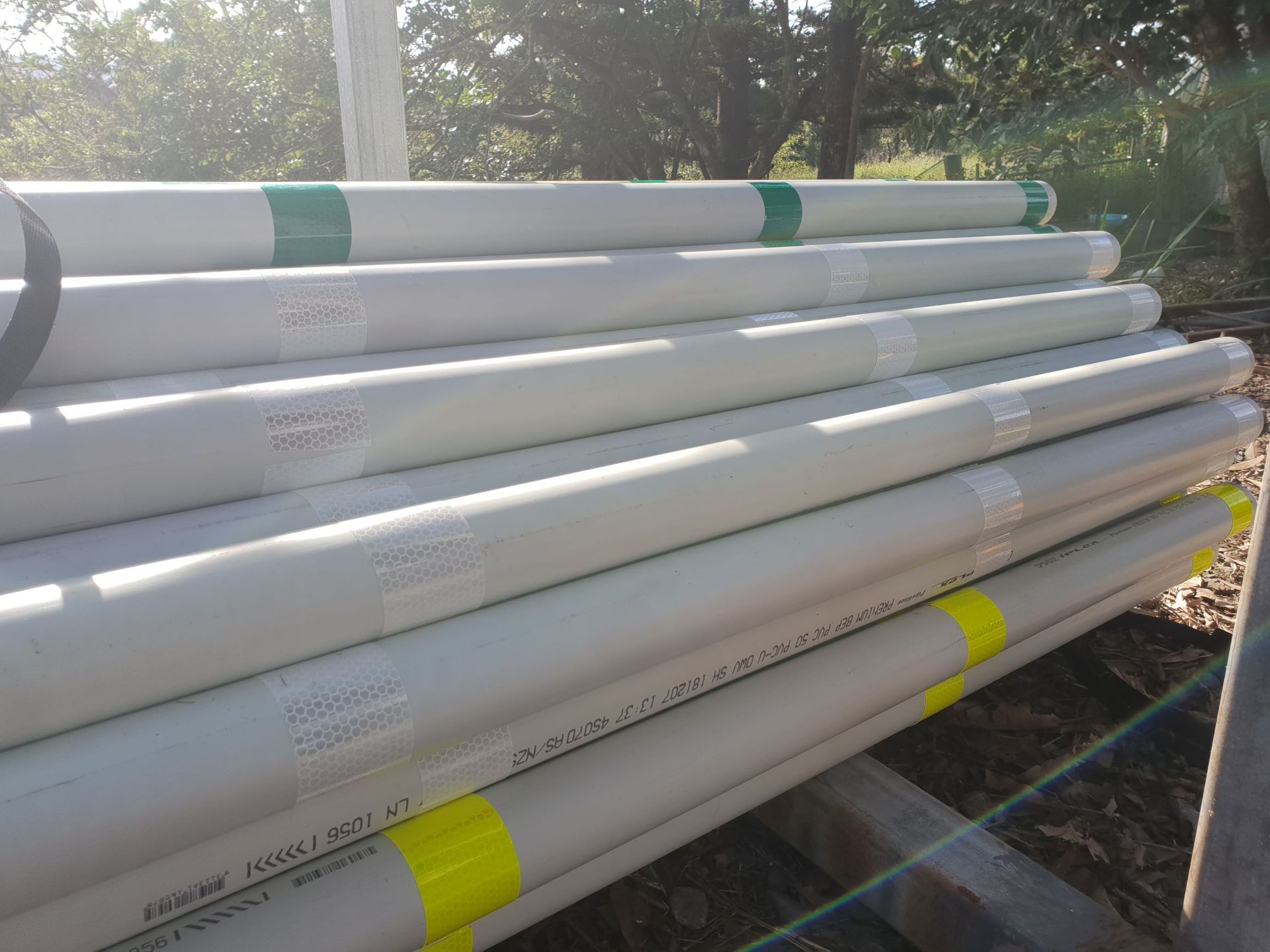 A stack of grey pipes with green and yellow identifying tape labels, resting outdoors on wooden supports.
