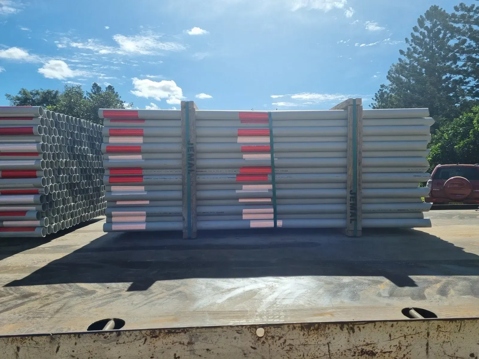 Stacks of grey metal scaffolding tubes with red and white stripes, on a flatbed truck in daylight.