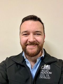A man with a beard is wearing a black jacket and smiling for the camera.