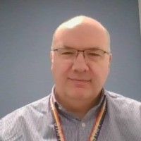 A bald man wearing glasses and a lanyard is smiling for the camera.