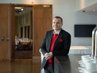 A man in a suit and red sweater is standing next to a counter.