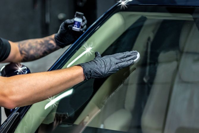 Technician cleaning and polishing a car windshield surface.