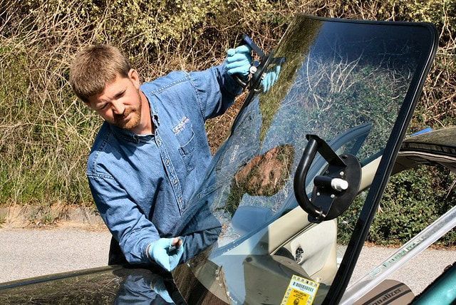 Technician carefully removing a damaged windshield from a car.