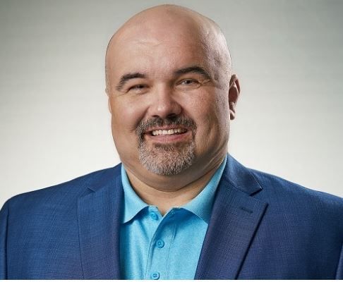 A bald man with a beard is wearing a blue suit and smiling.