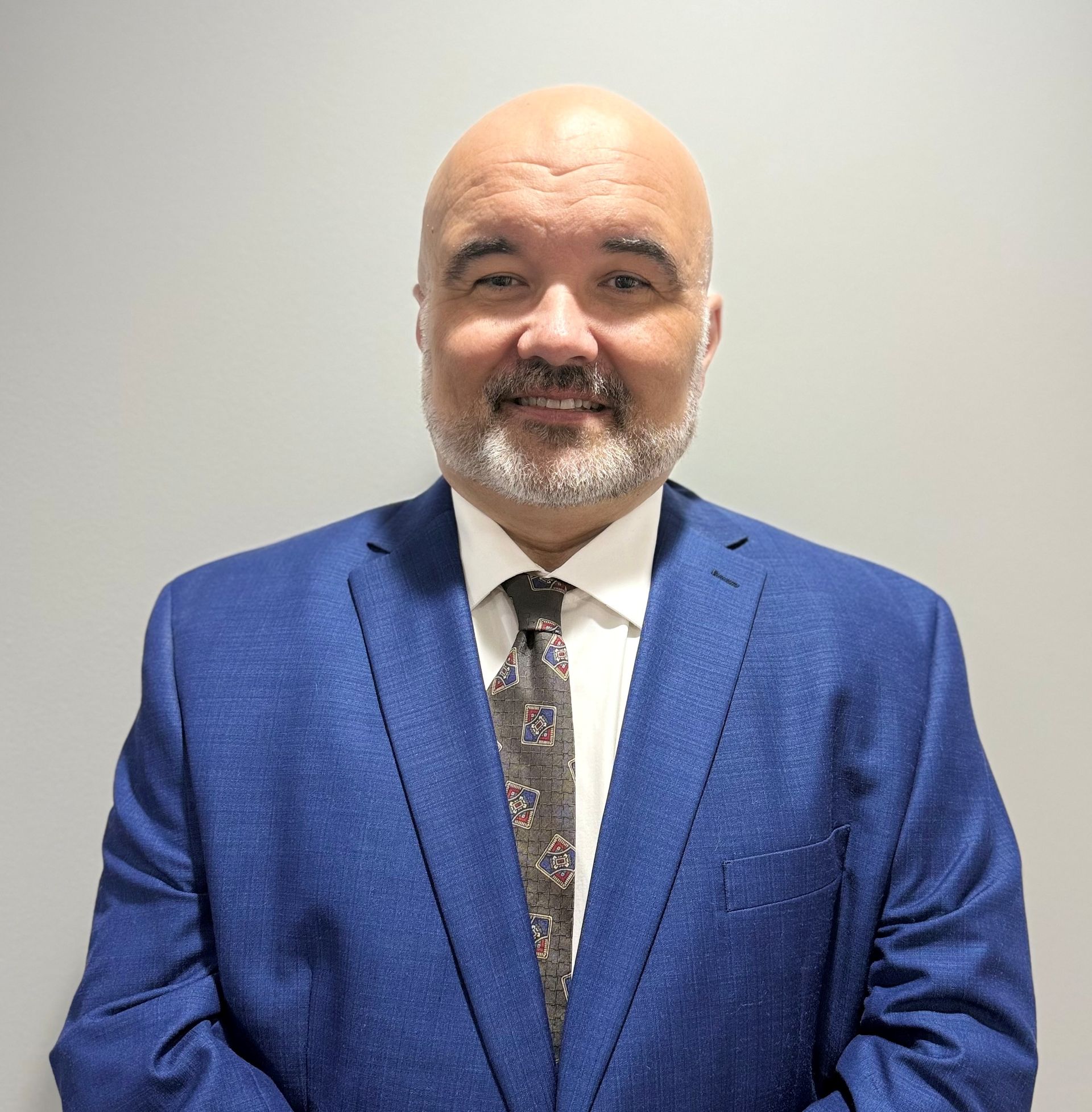 A bald man with a beard is wearing a blue suit and smiling.