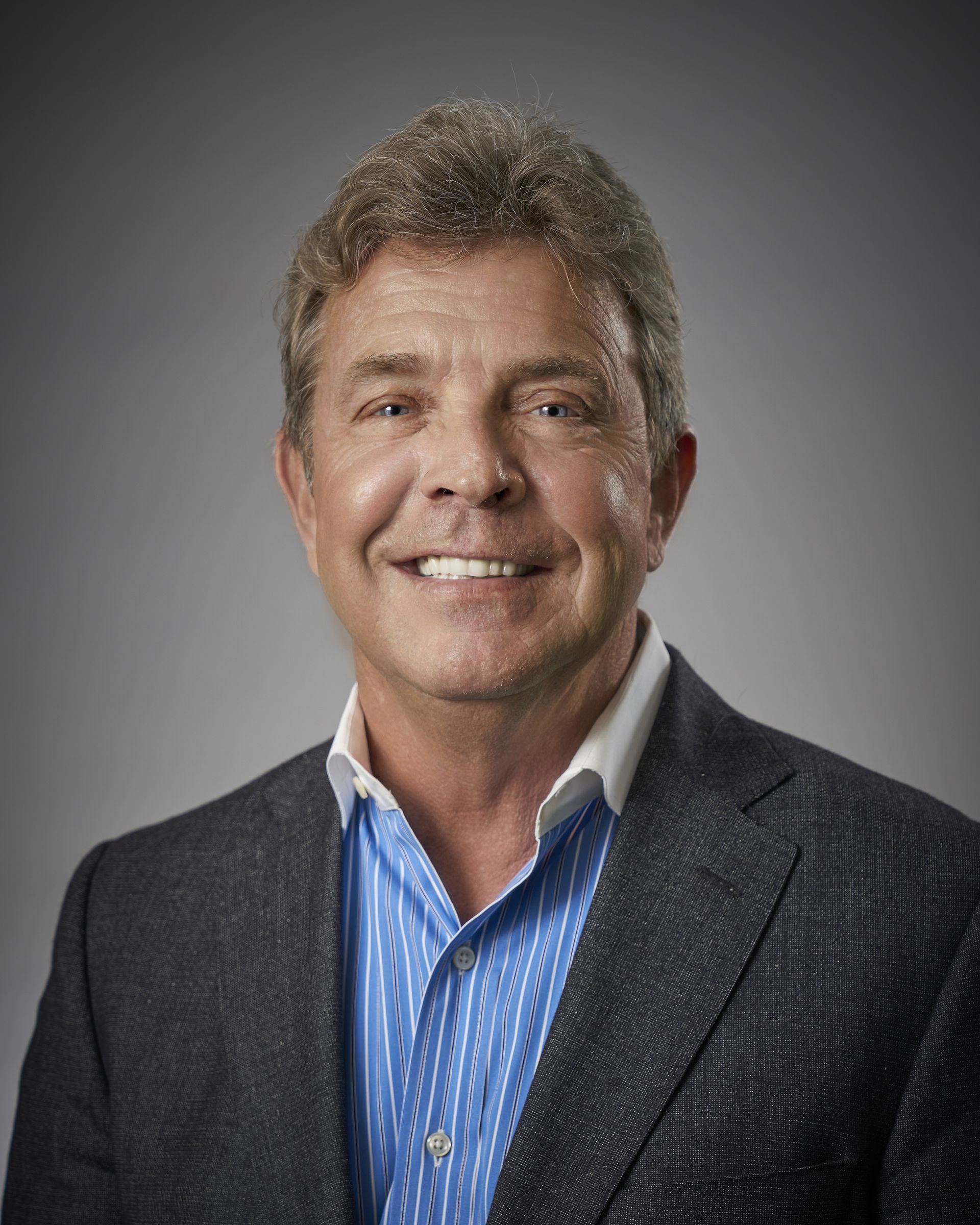 A man in a suit and blue striped shirt is smiling for the camera.