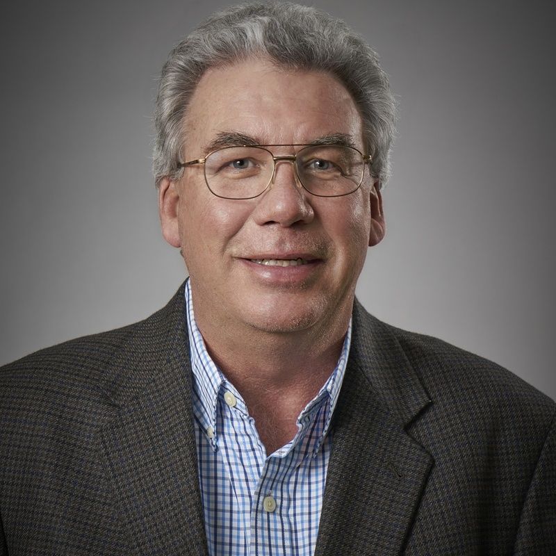 A man wearing glasses and a suit is smiling for the camera