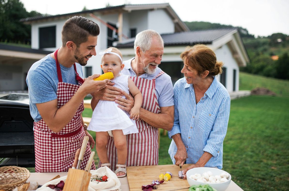 A family is standing around a table preparing food in front of a house.