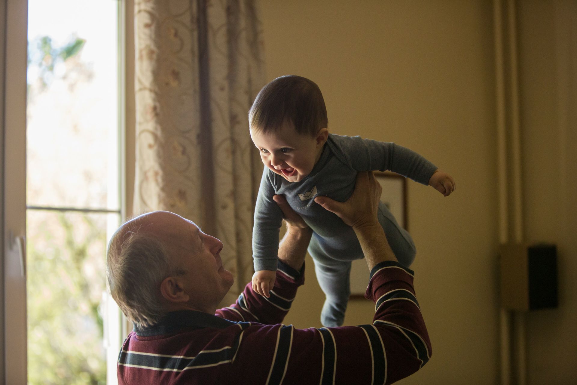 An elderly man is holding a baby in the air.