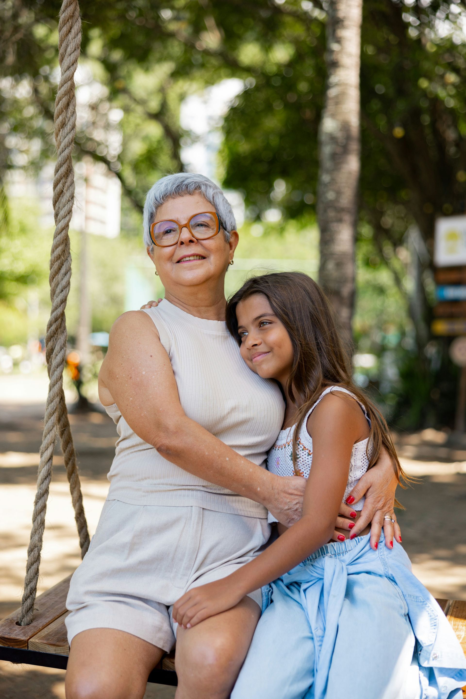 An elderly woman and a young girl are sitting on a swing.