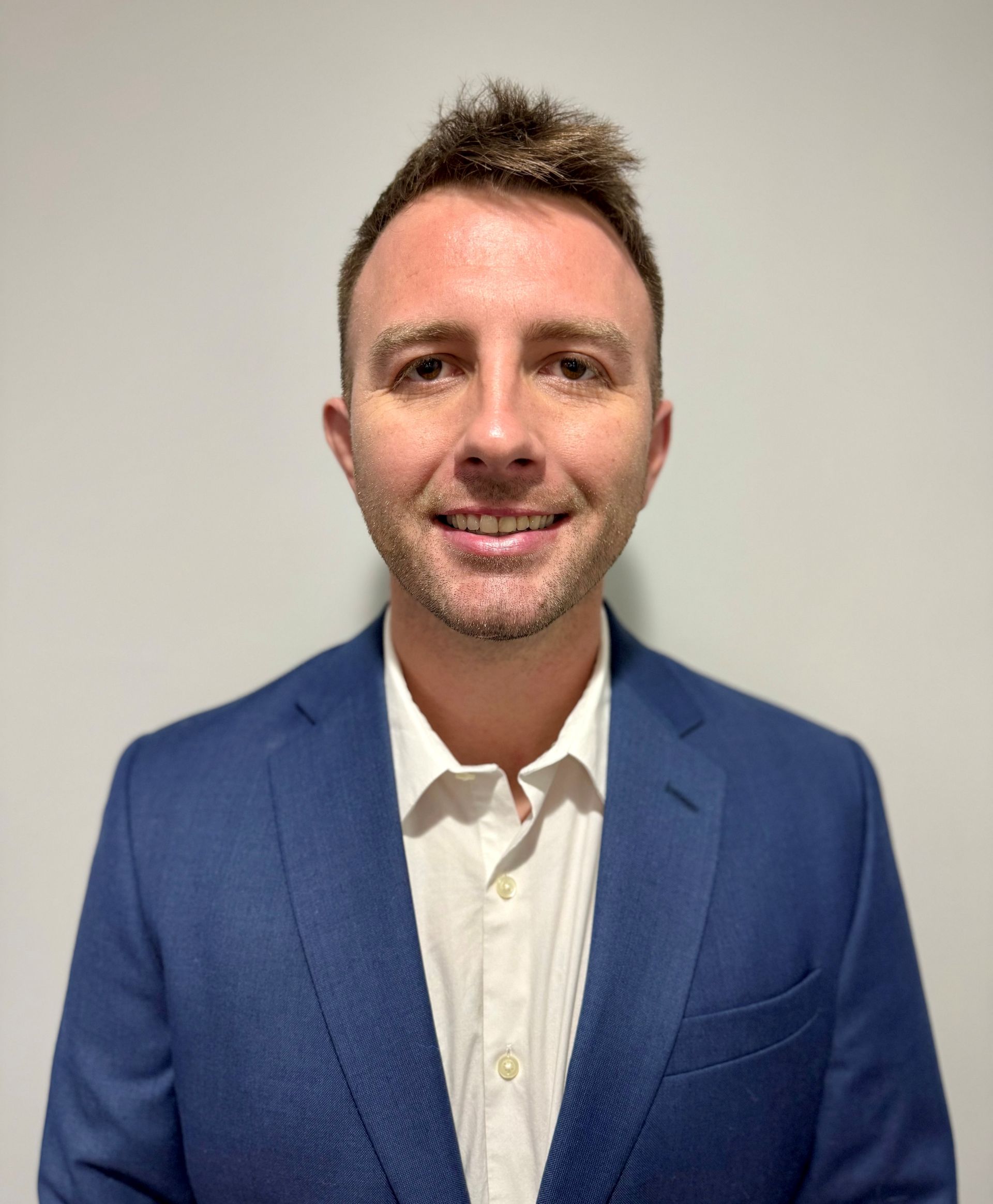 A bald man with a beard is wearing a blue suit and smiling.