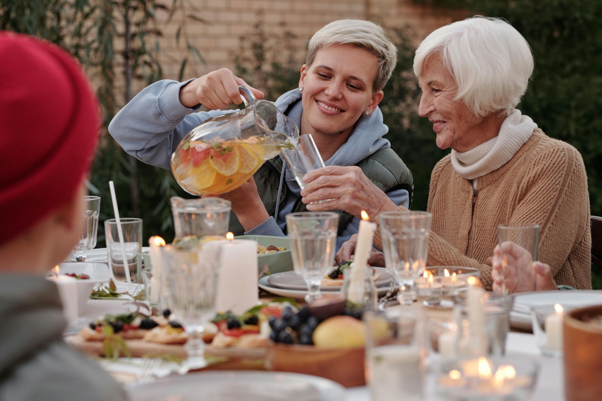 A woman is pouring a drink into a glass at a dinner table.