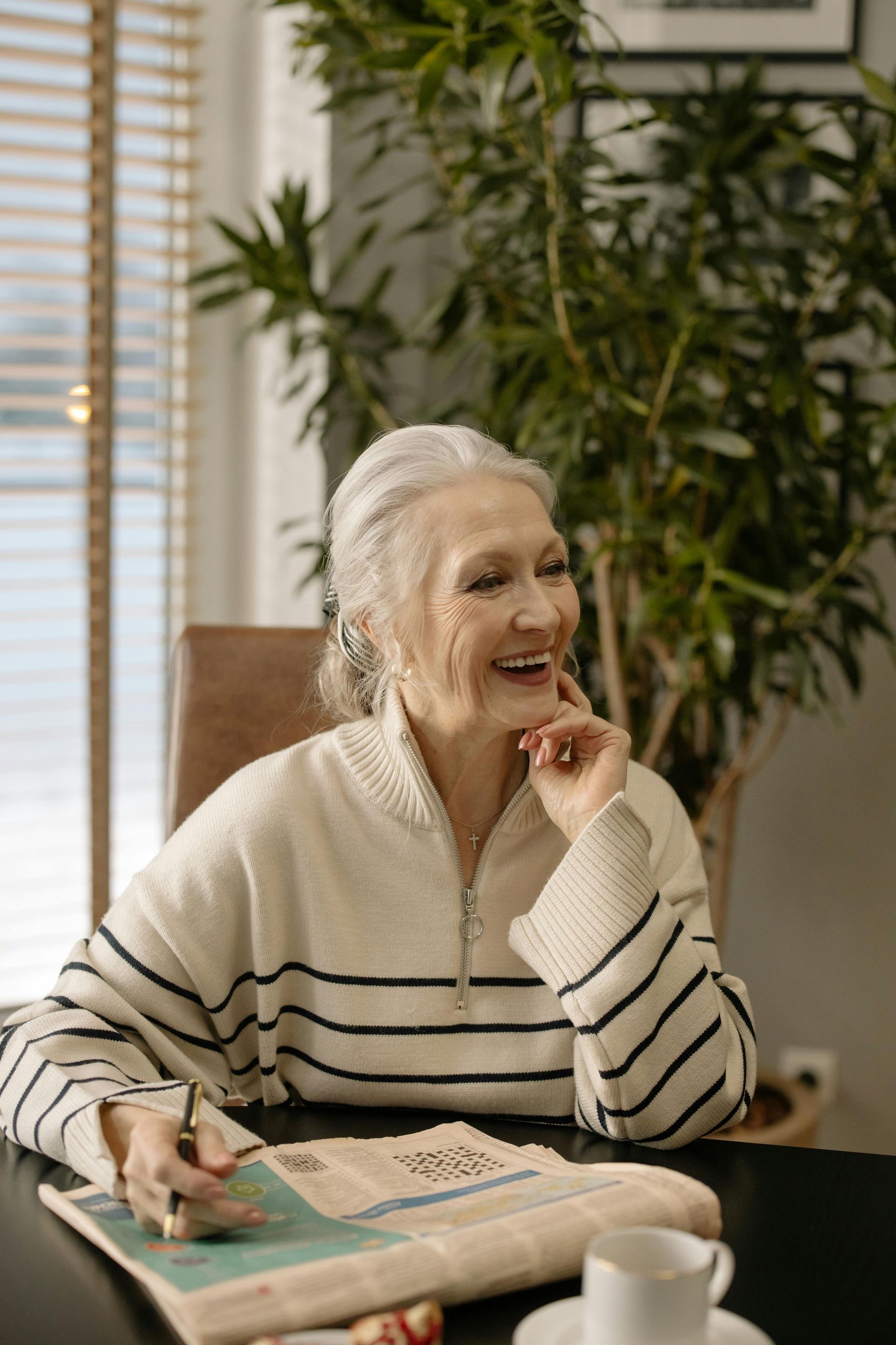 An elderly woman is sitting at a table writing in a notebook.