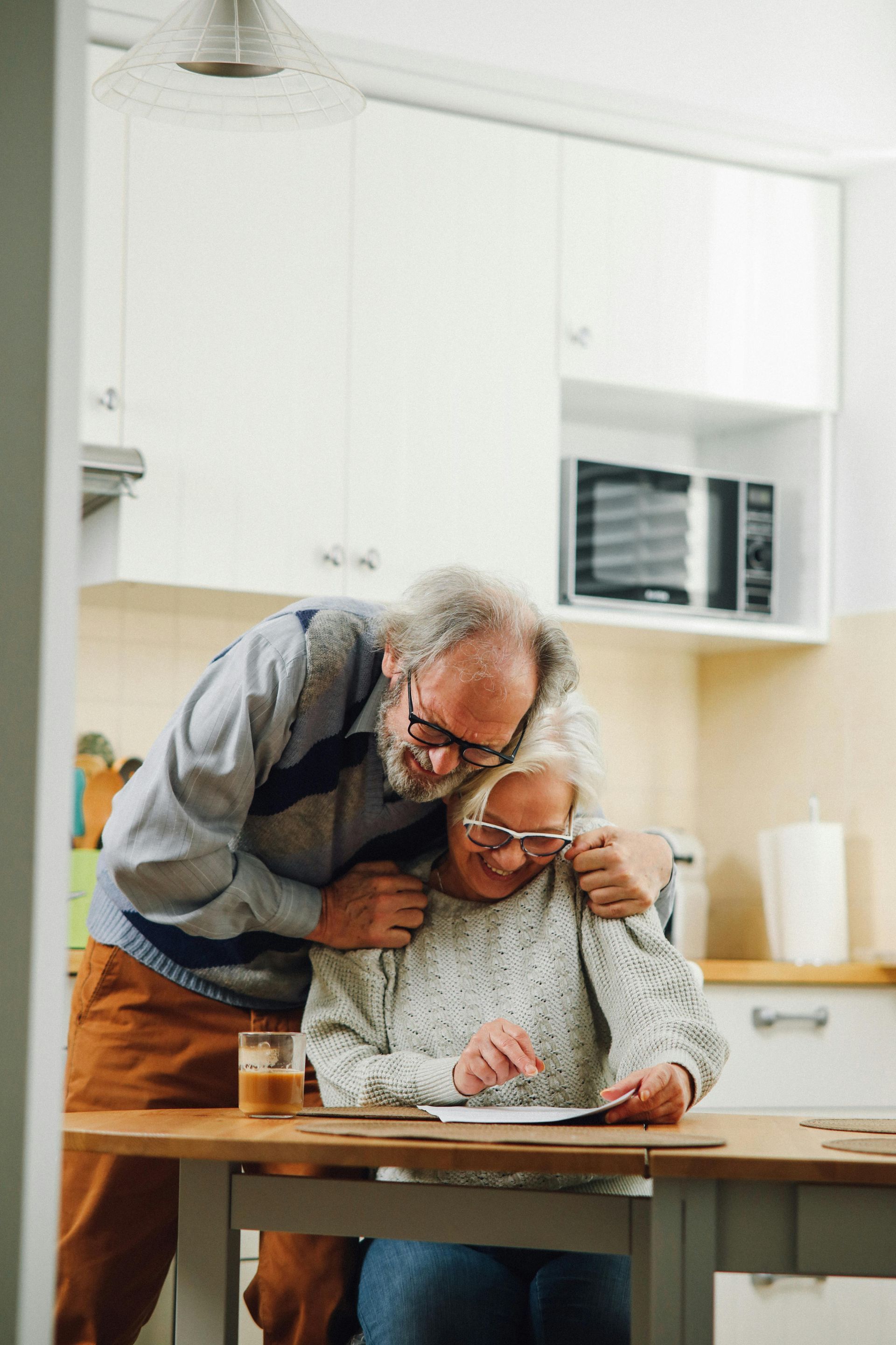 An elderly couple is sitting at a table in a kitchen.