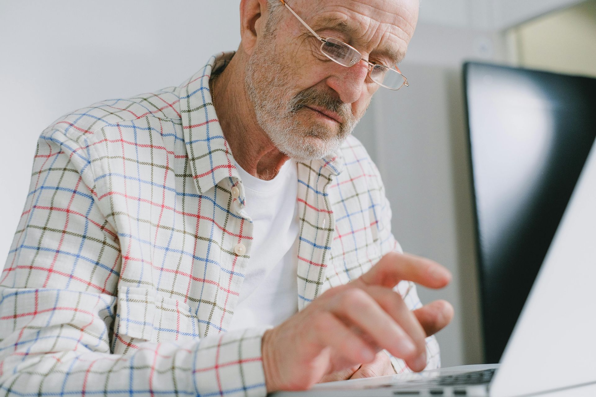 An older man wearing glasses is using a laptop computer.