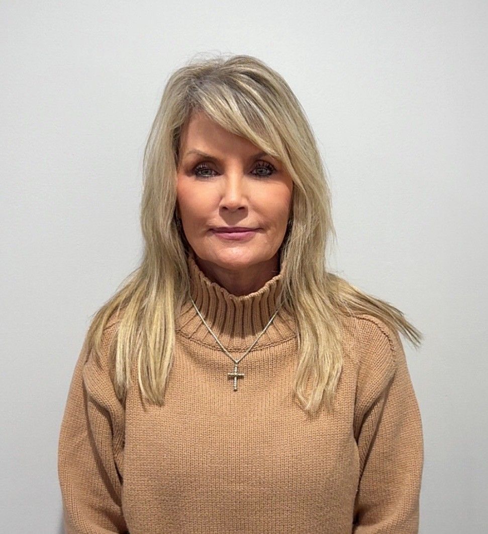 A woman in a blue jacket and white shirt is smiling for the camera