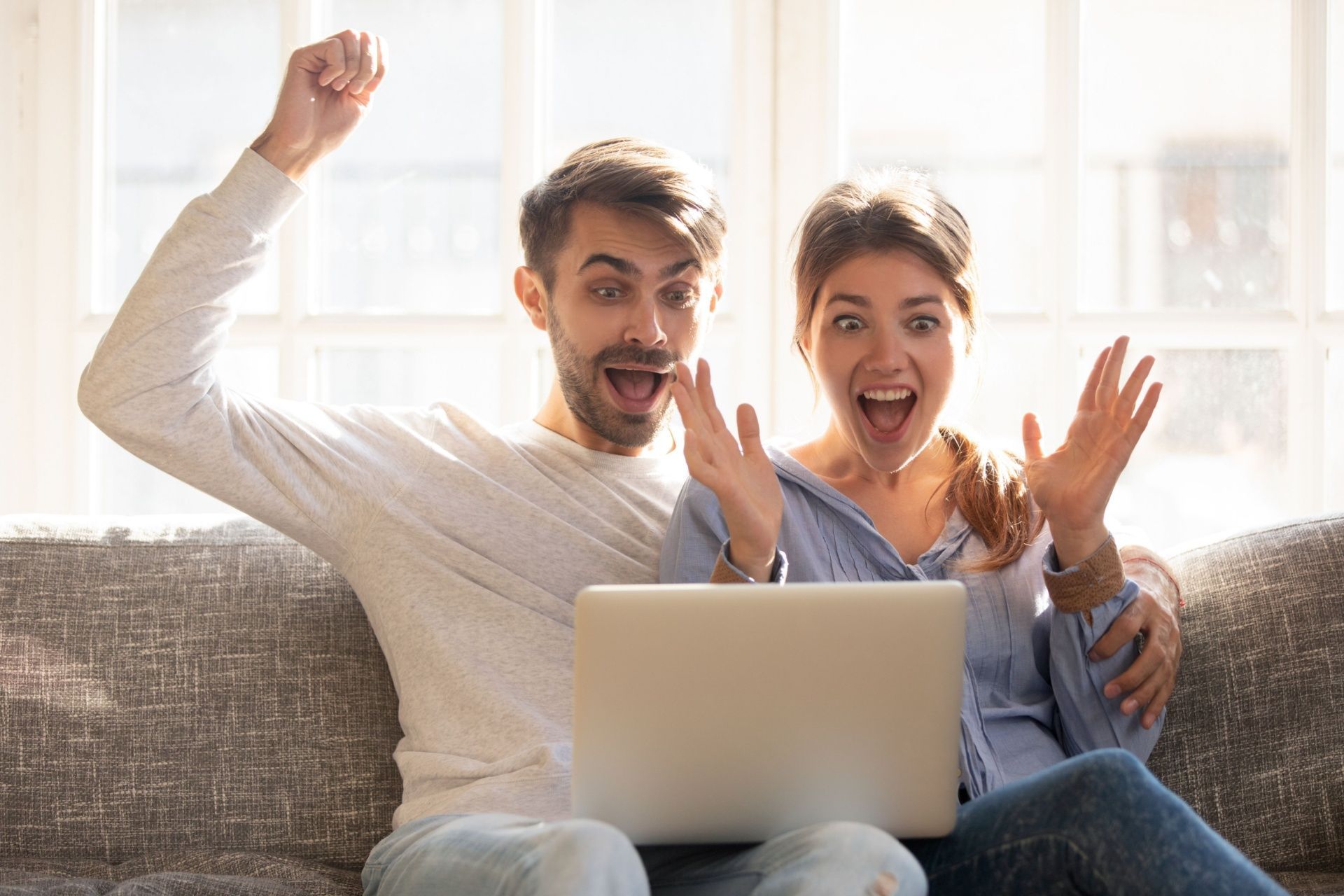 A man and a woman are sitting on a couch looking at a laptop computer.