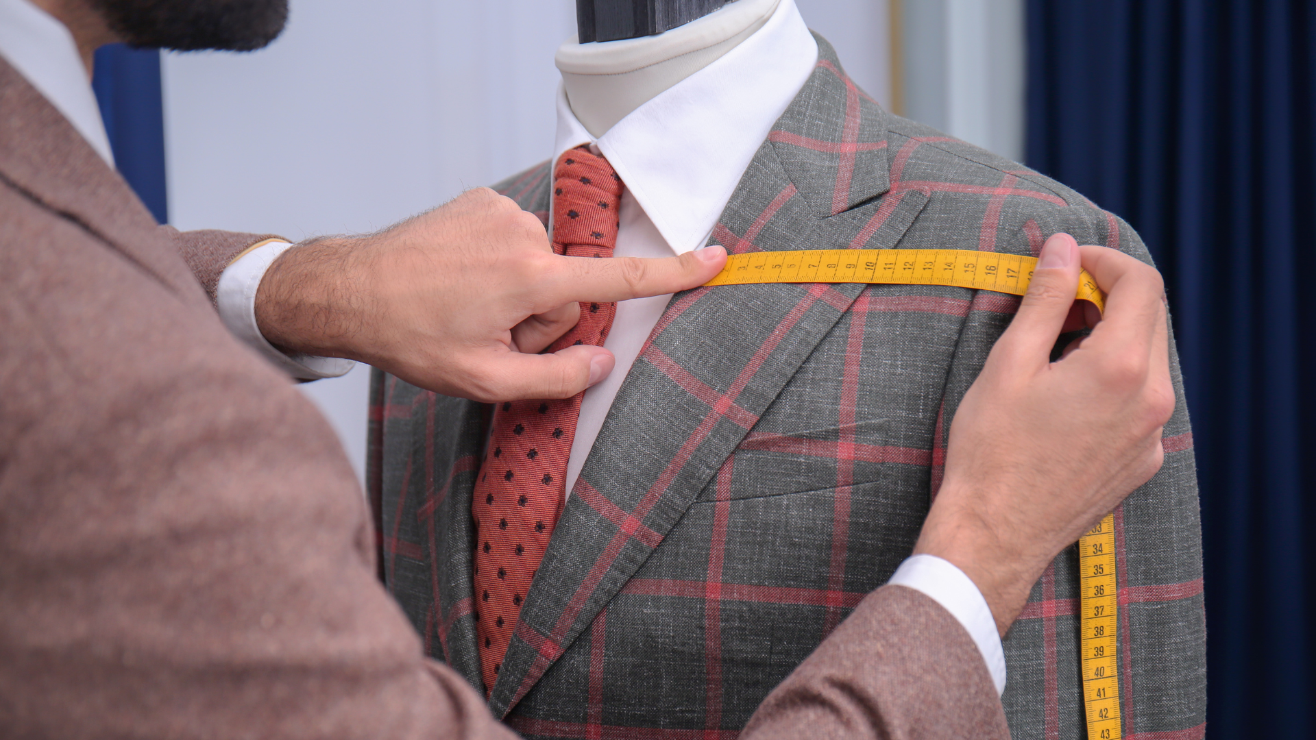 A man is measuring the shoulder of a suit on a mannequin.