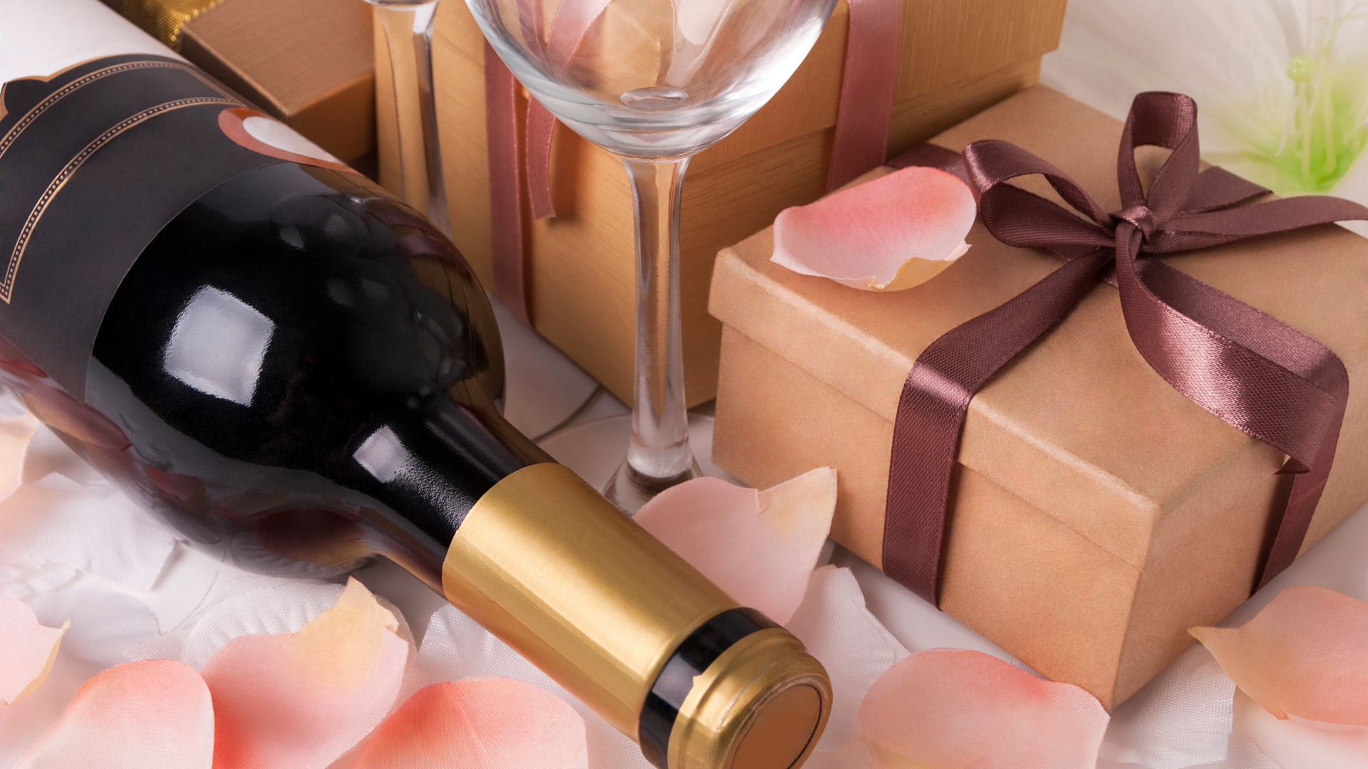 A bottle of wine is surrounded by gifts and petals