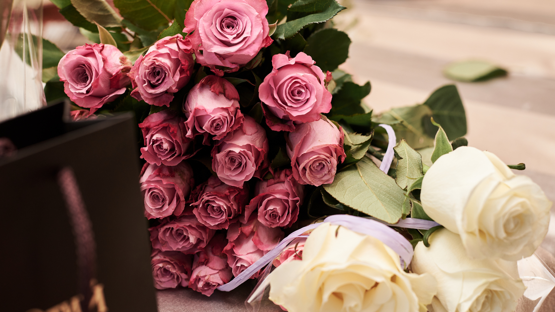 A bouquet of pink and white roses next to a black bag