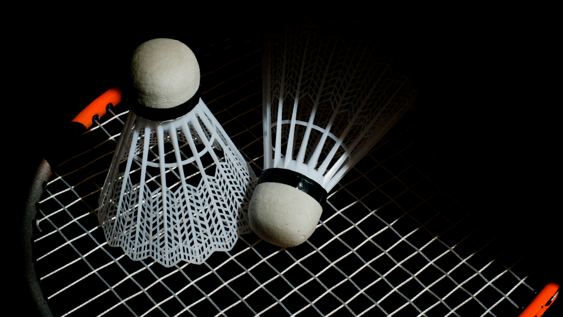 Two badminton shuttlecocks are sitting on top of a badminton racket.
