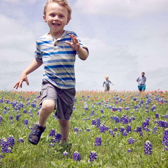 A young boy is running through a field of purple flowers