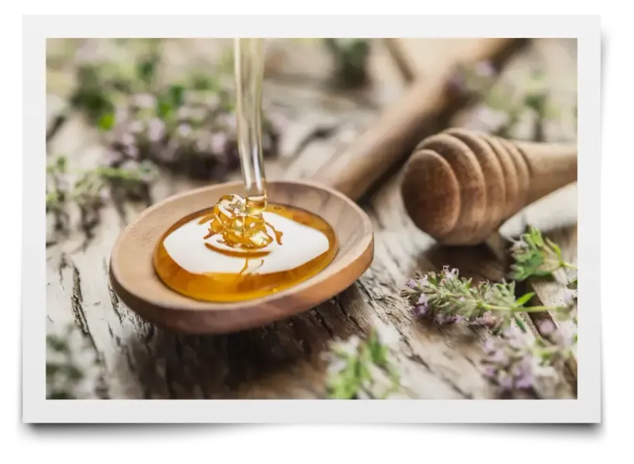 A jar of honey with a honey dipper next to a honeycomb
