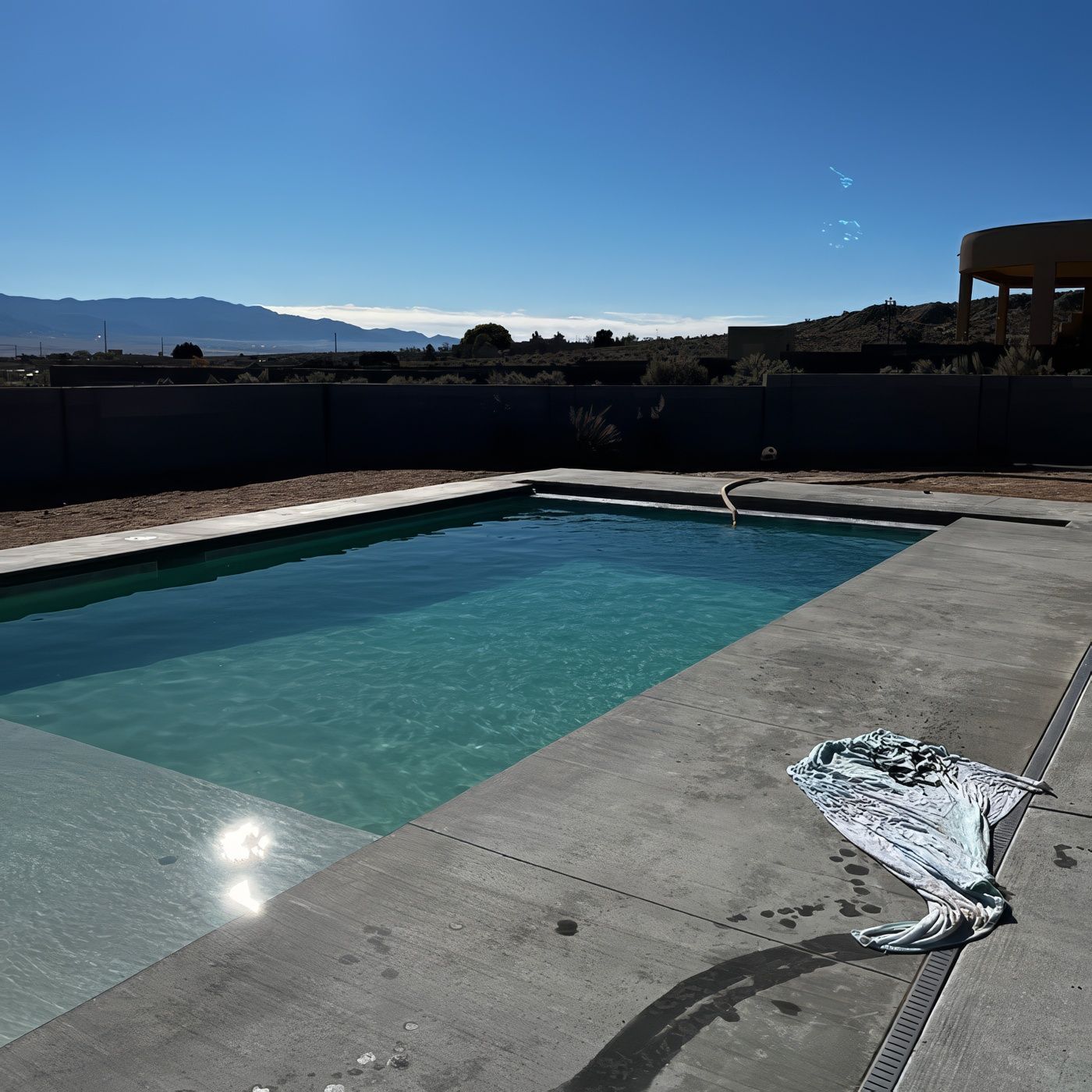 Backyard swimming pool with turquoise water, concrete deck, and mountains under a clear blue sky