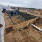 Construction site with workers pouring concrete into a foundation trench near wooden forms.