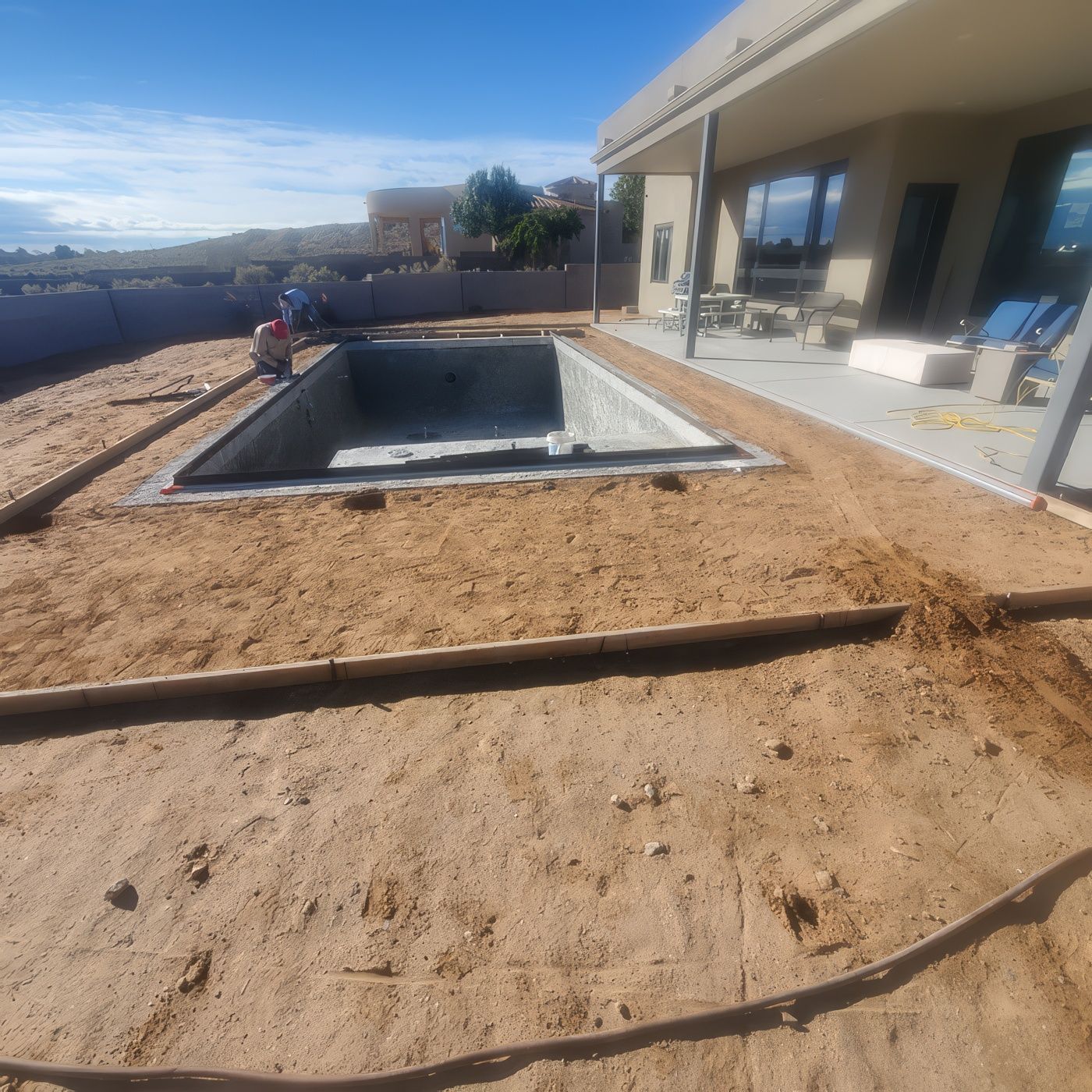 Backyard patio with an empty rectangular pool under construction beside a house