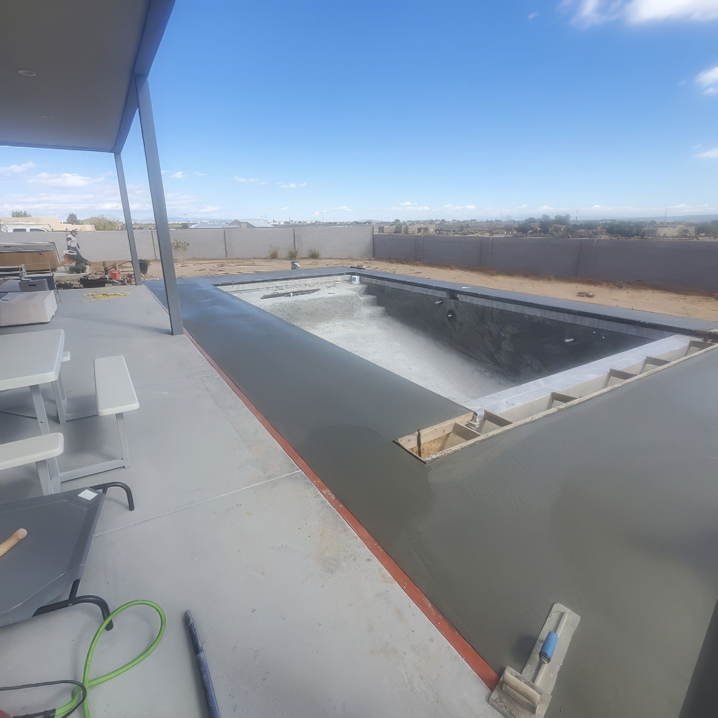 Freshly poured wet concrete surrounds an unfinished backyard swimming pool on a sunny day.
