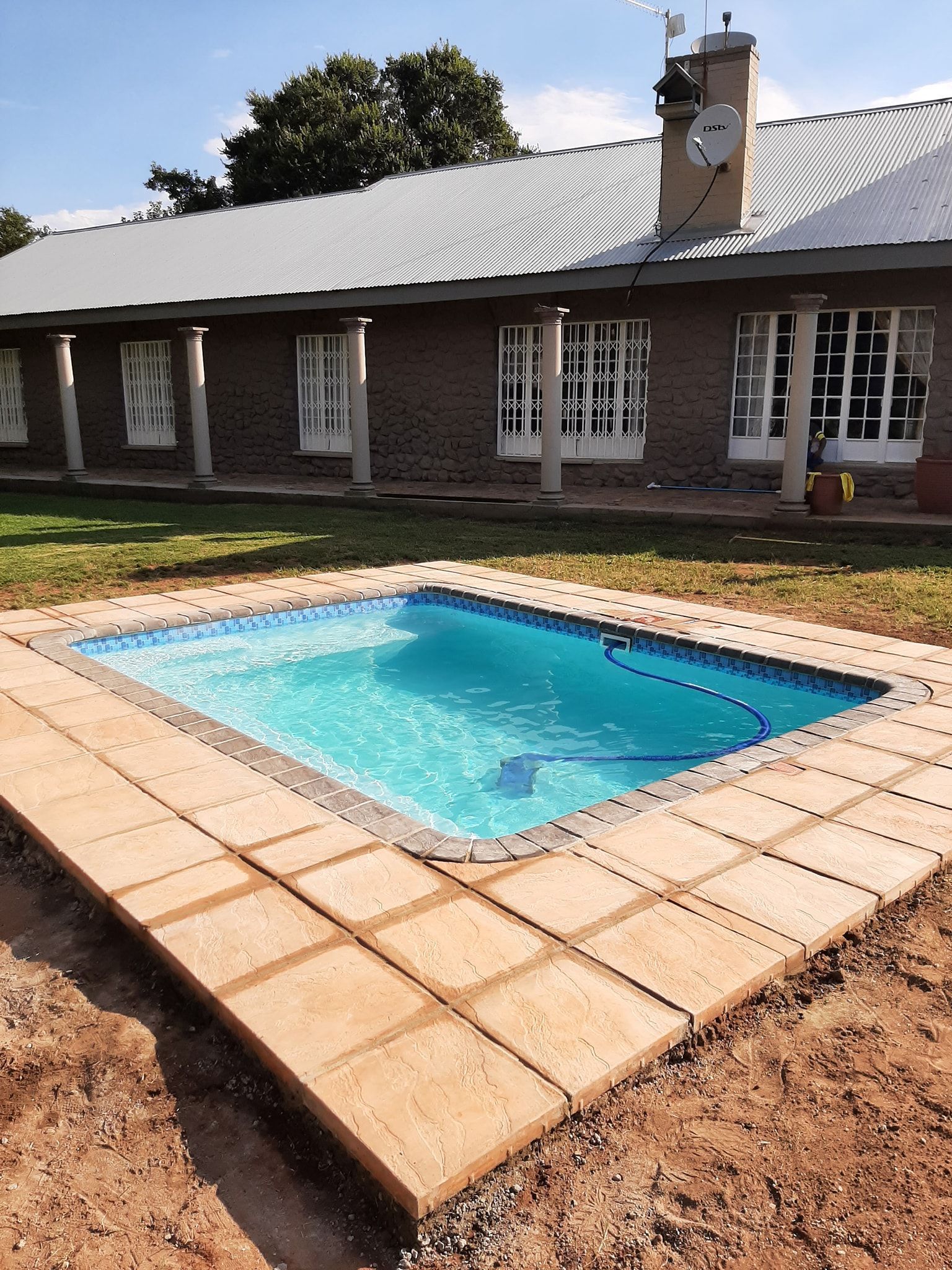 Backyard swimming pool with blue water beside a single-story house and tiled patio