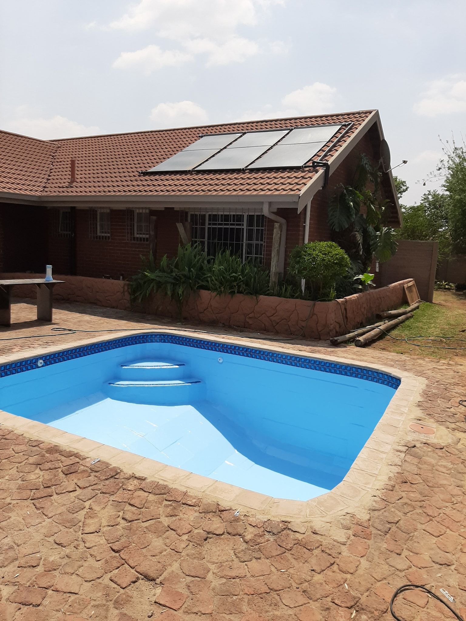 Backyard swimming pool beside a brick house with solar panels on the roof