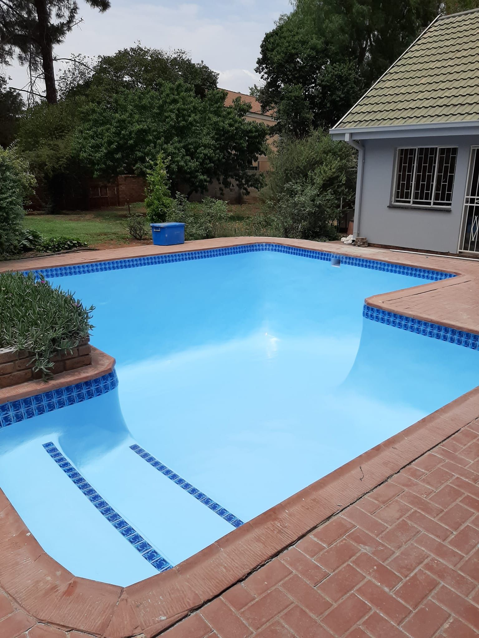 Backyard swimming pool with blue water, brick patio, and a house in the background