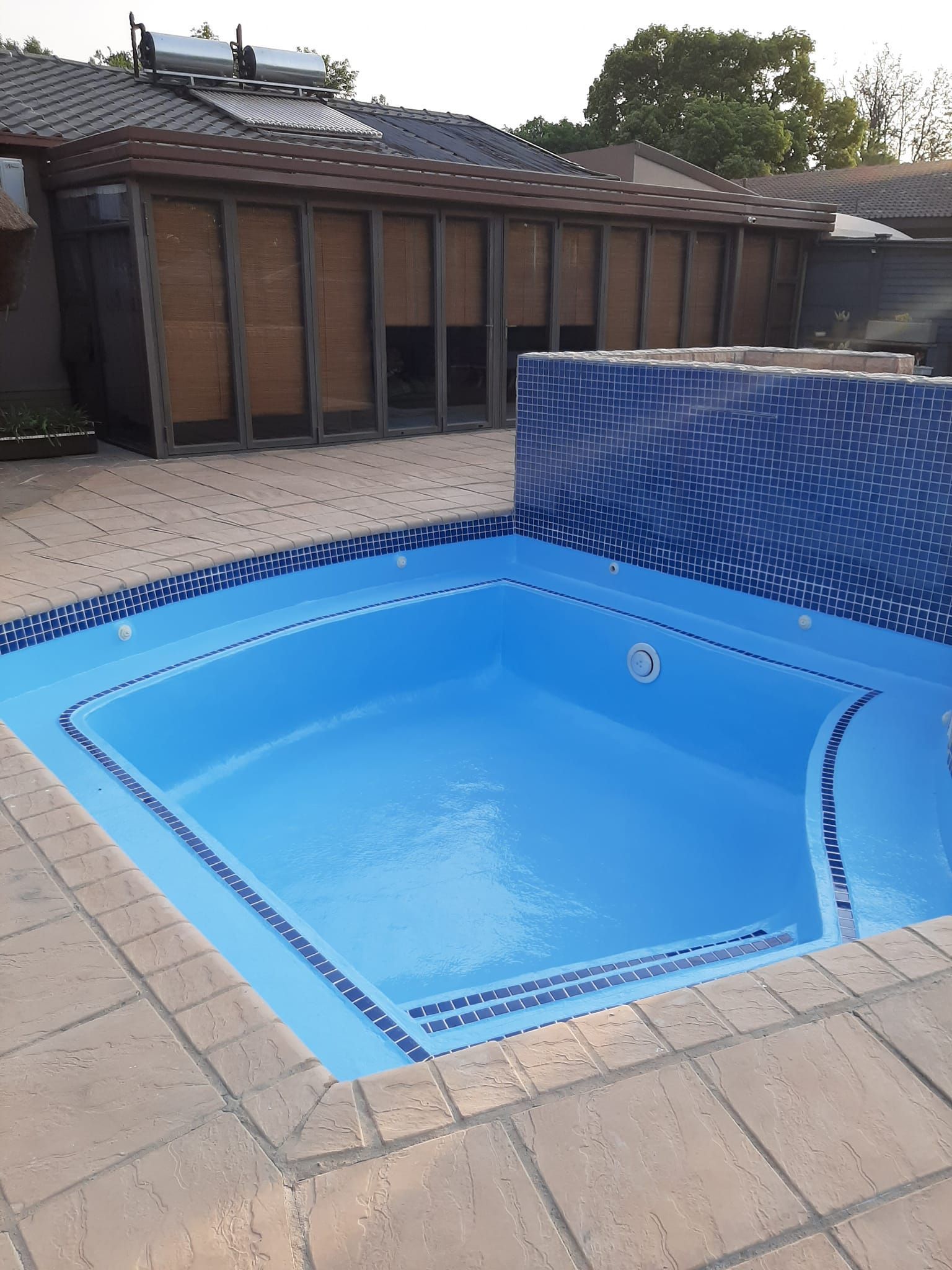 Empty blue tiled hot tub beside a pool deck, with a wood-paneled building in the background