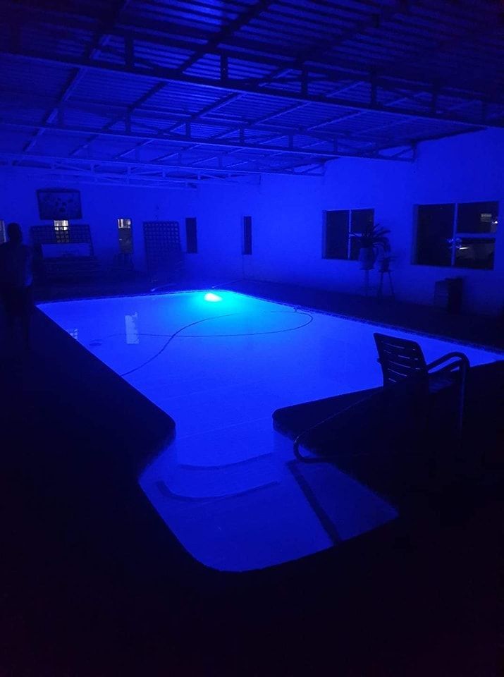 An indoor swimming pool at night, illuminated by bright blue underwater lights in a dark, enclosed setting.