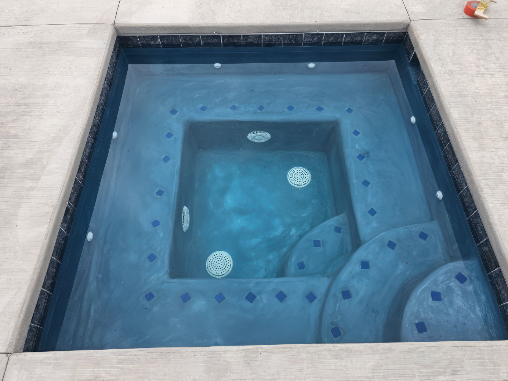 Blue tiled spa or hot tub viewed from above, with circular jets and a curved bench seat