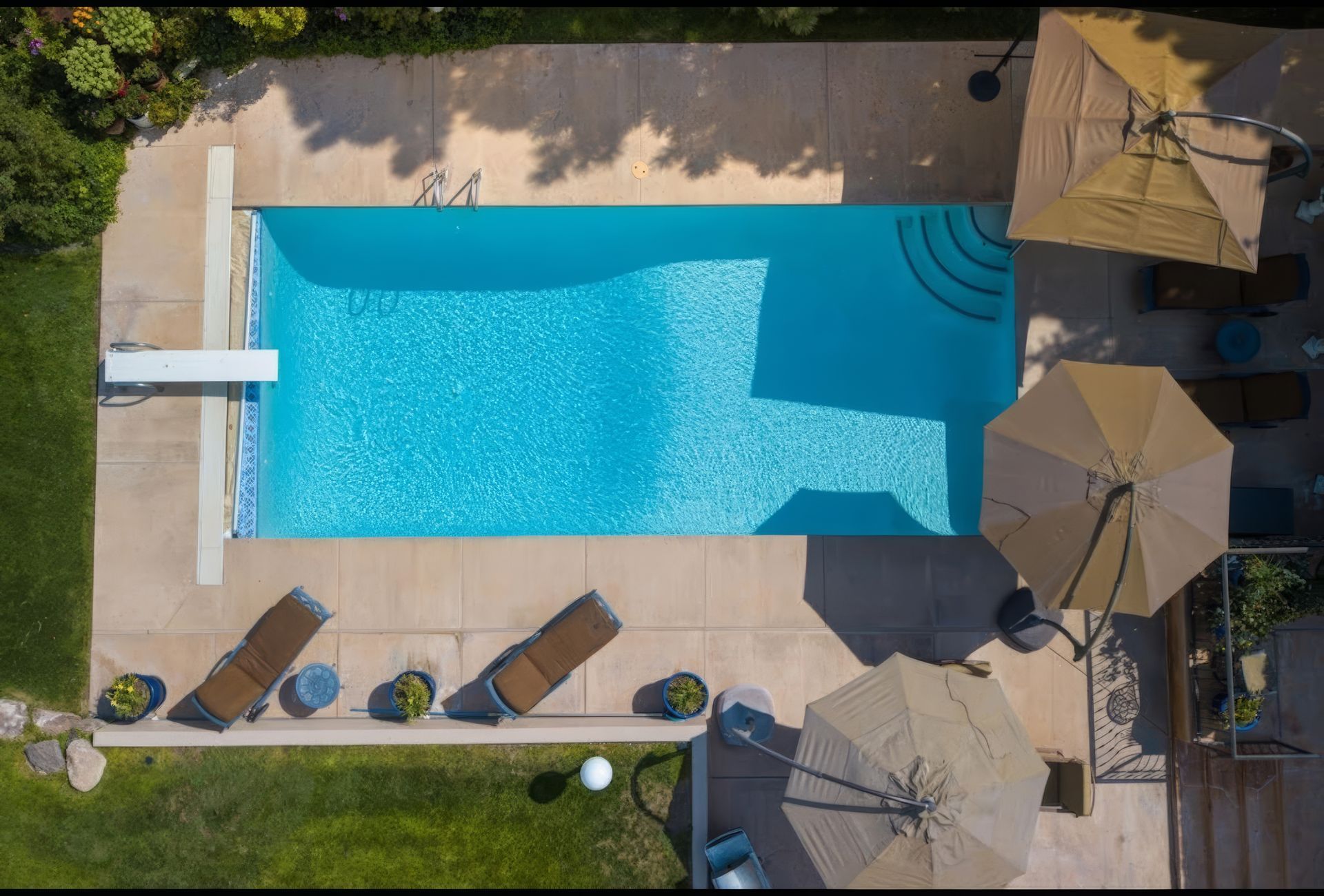Overhead view of a turquoise swimming pool with lounge chairs and umbrellas on a sunny patio