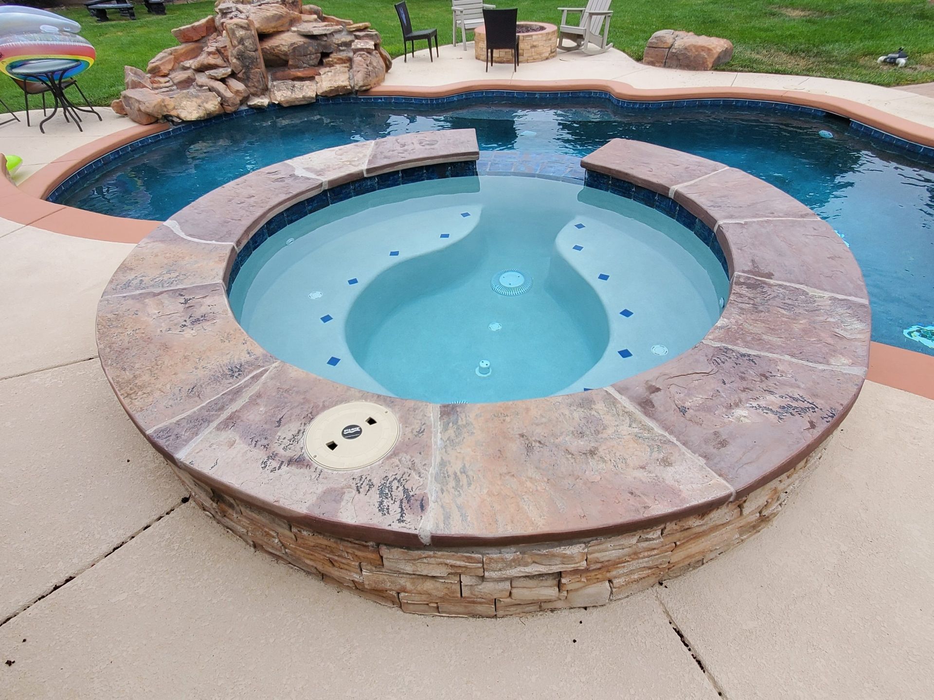 Backyard swimming pool with a circular hot tub and tan stone coping, viewed from above