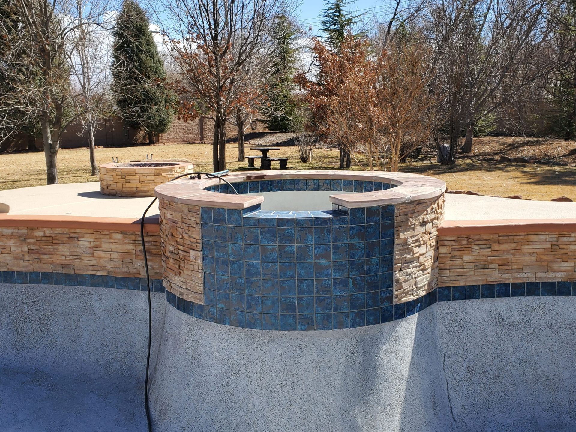 Backyard pool with a raised blue-tile water feature and stone coping amid trees.