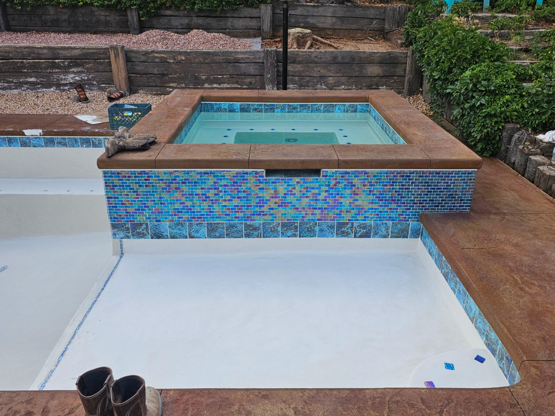 Backyard patio with an empty white pool, blue-tiled spa, and terracotta steps with greenery around it