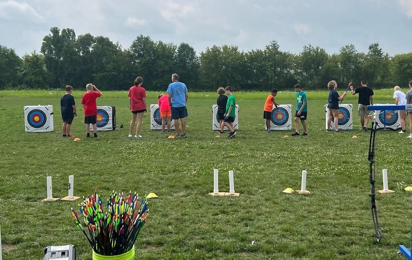 A group of people are standing in a field in front of archery targets.