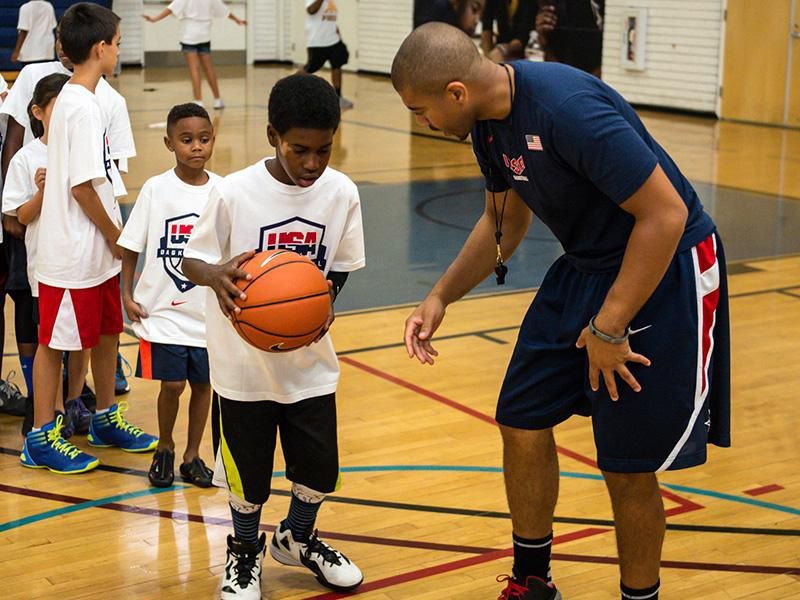 A man in a basketball gym gives high-fives to a group of children.