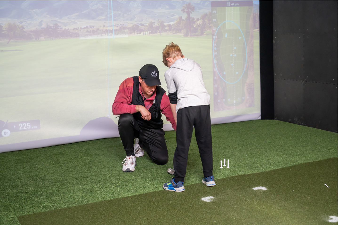 A man and a boy are playing golf in a simulator.