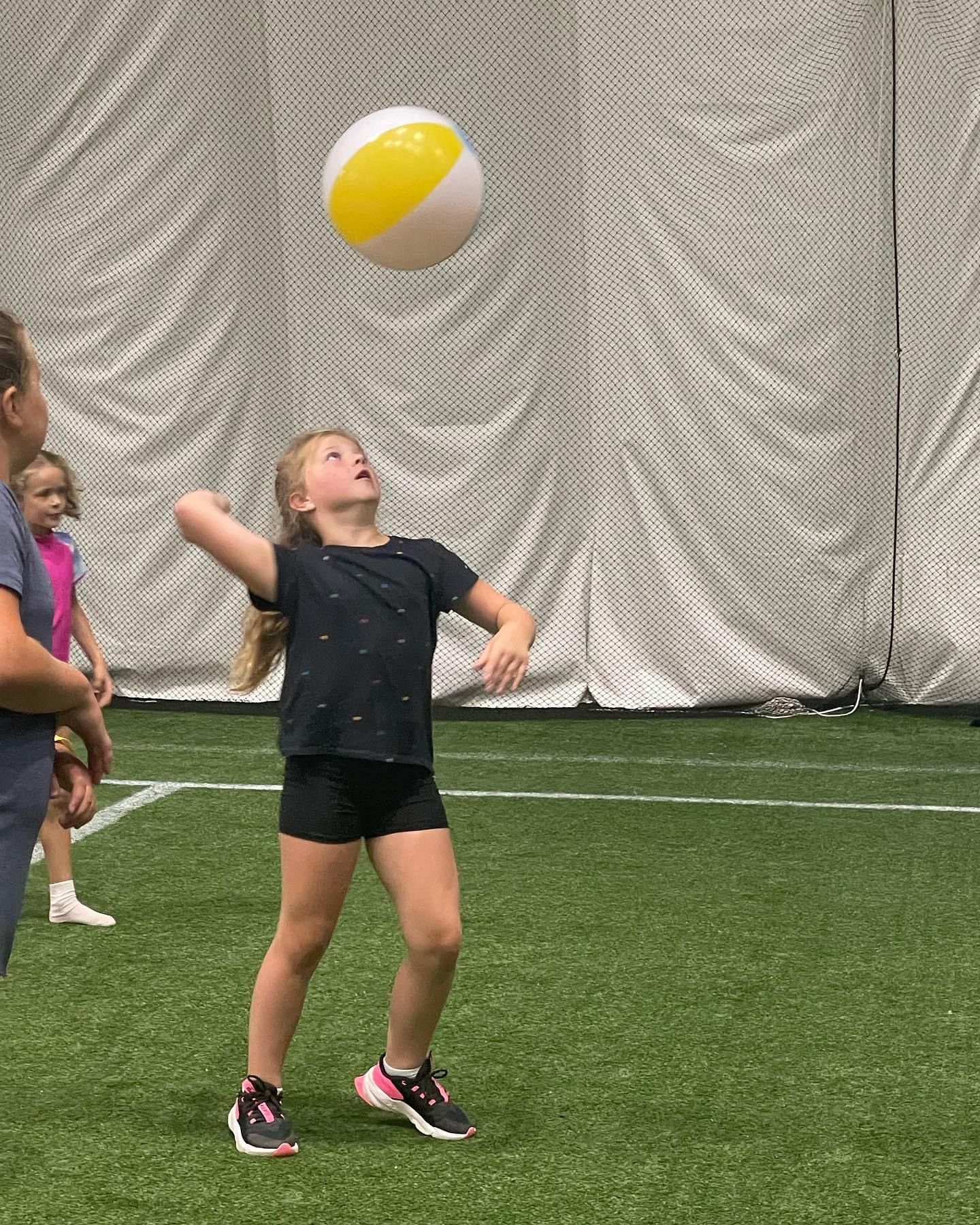 A little girl is playing with a beach ball on a field.