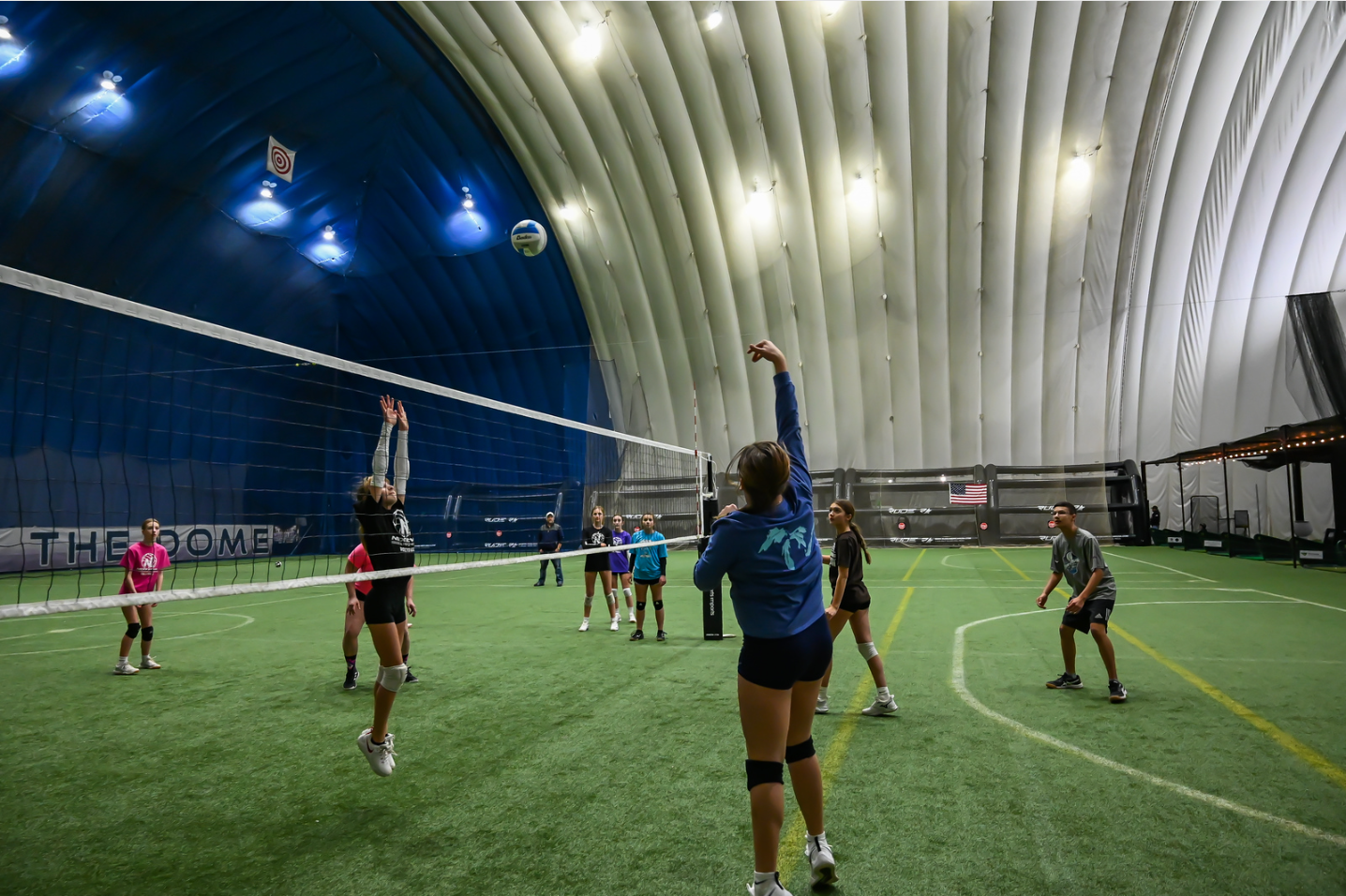 A group of people are playing volleyball in an indoor gym.